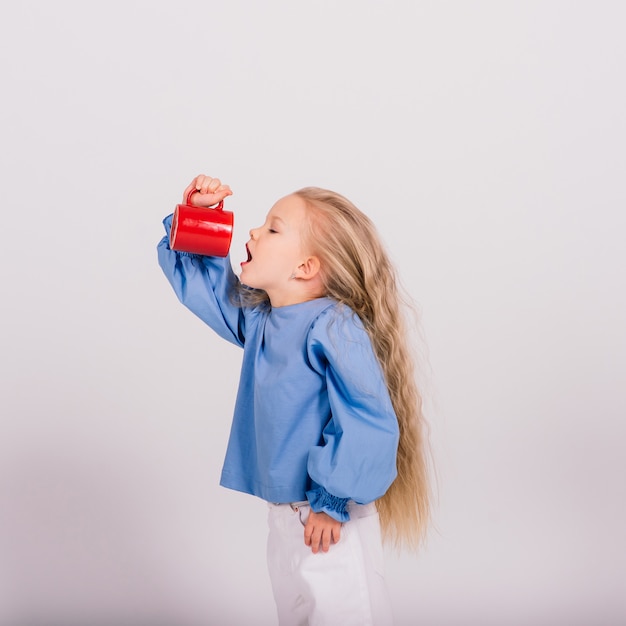 Kleines lächelndes Kindermädchen, das Tasse hält, lokalisiert über weißem Hintergrund. Studioaufnahmen