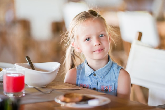 Kleines lächelndes Mädchen, das Café im im Freien zu Mittag isst