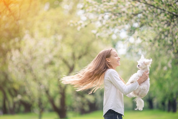 Kleines lächelndes Mädchen, das Welpen im Park spielt und umarmt