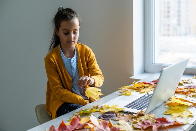 Kleines lächelndes Mädchen mit Laptop um Herbstlaub