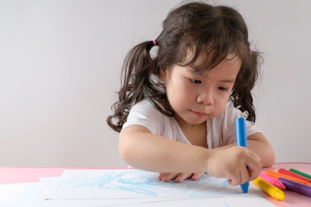 Kleines lockiges asiatisches Mädchen genießt das Zeichnen zu Hause. Bildungskonzept.