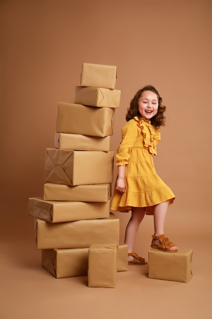 Kleines lockiges Mädchen mit großem Stapel von Geschenken für den Feiertag