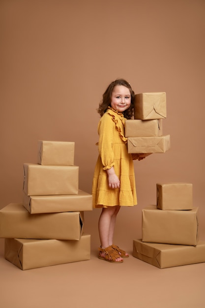 Kleines lockiges Mädchen mit großem Stapel von Geschenken für den Feiertag