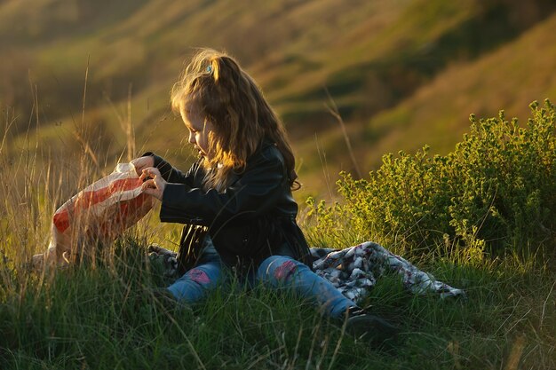 Kleines lockiges Mädchen mit ihrer Familie bei einem Picknick außerhalb der Stadt bei Sonnenuntergang