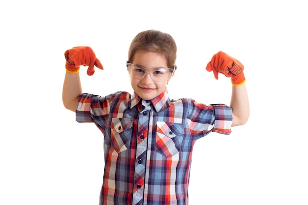 Kleines lustiges Mädchen mit langem kastanienbraunem Zopf in kariertem rotem Hemd mit orangefarbenen Handschuhen und Brille