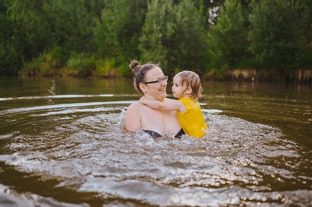 Kleines lustiges süßes blondes Mädchen Kleinkind im gelben Body lachen lernt draußen schwimmen um