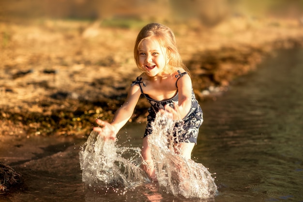 kleines Mädchen am Fluss im Sommer spritzt Wasser