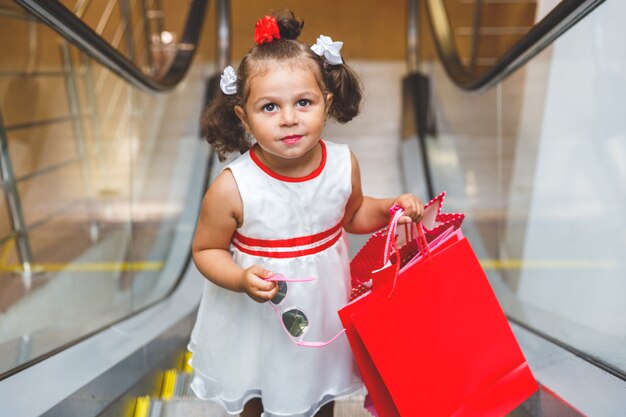 Kleines Mädchen auf der Rolltreppe im Einkaufszentrum mit bunten Taschen