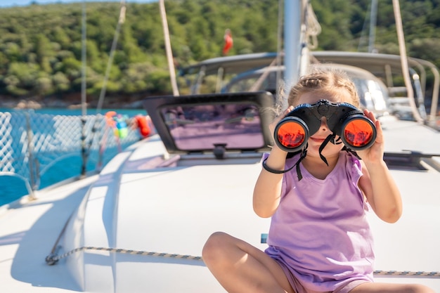 Kleines Mädchen auf einer Yacht, das durch ein Fernglas im Meer blickt