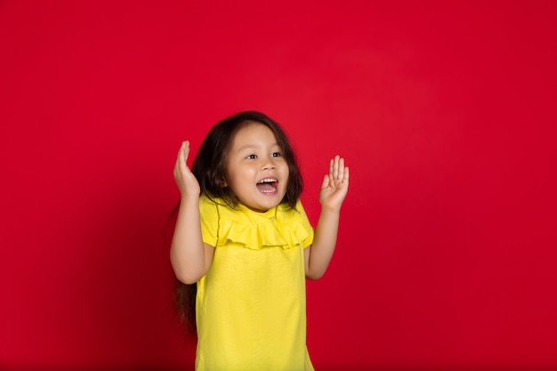 Kleines Mädchen auf rotem Hintergrund isoliert, glücklich