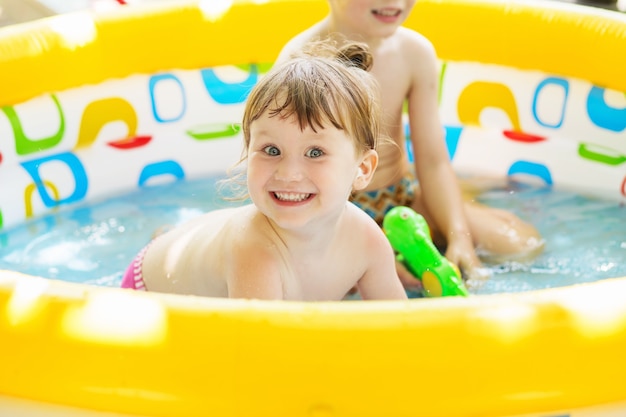 Foto kleines mädchen badet im gelben aufblasbaren schwimmpaddelbecken draußen im heißen sommertag. kinder im schwimmbad