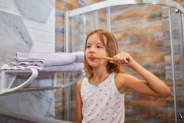 Kleines Mädchen beim Zähneputzen mit Öko-Holzzahnbürste im Badezimmer zu Hause, gesundes Hygienekonzept