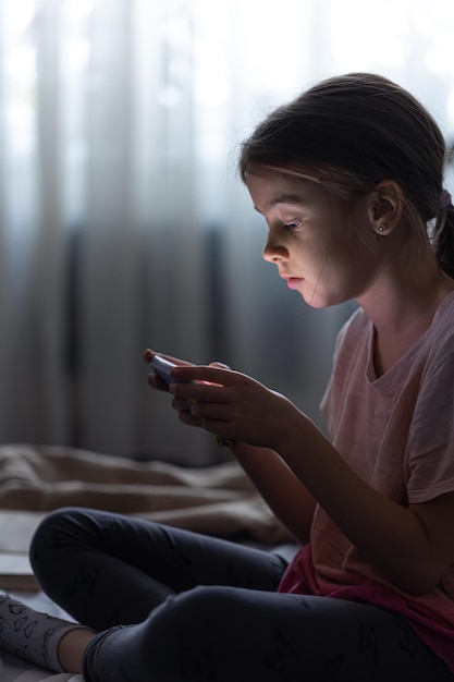 Kleines Mädchen benutzt das Telefon, während es abends im Bett sitzt