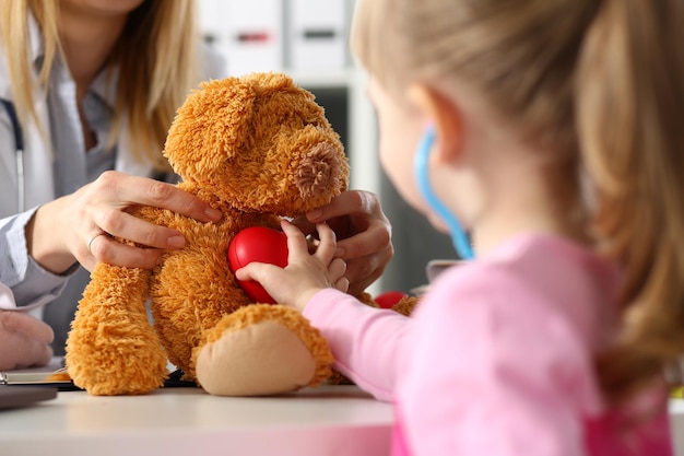 Kleines Mädchen berührt das Herz eines ausgestopften Teddybären und hört mit dem Herzschlag des Stethoskops