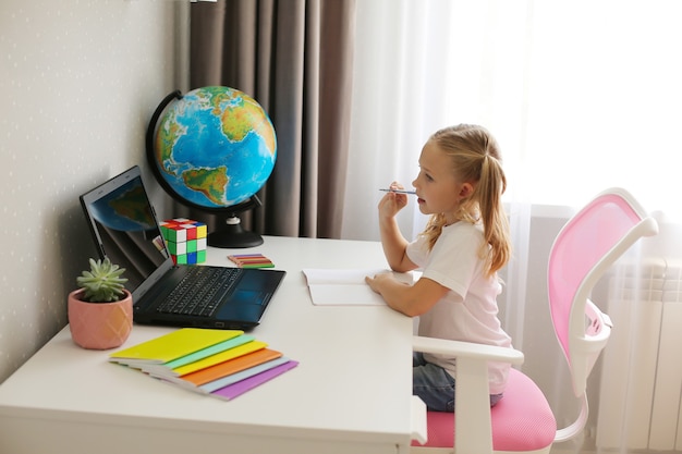 kleines Mädchen blondes Schulmädchen zu Hause unterrichtet Online-Schulungsnotizbücher Globus Laptop