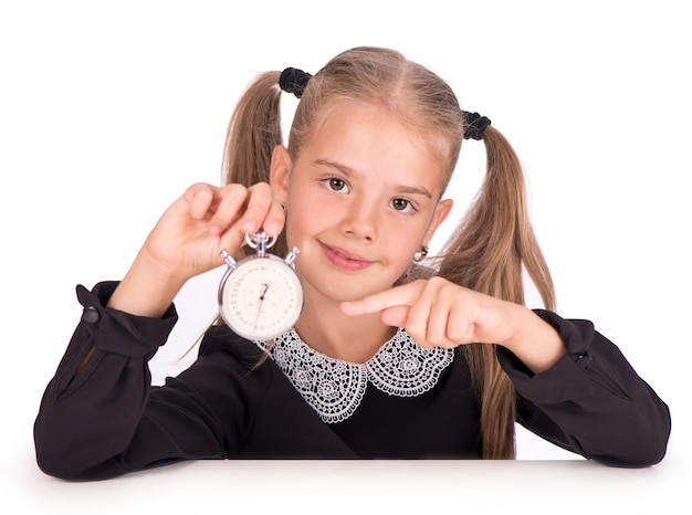 Kleines Mädchen, Blondine in einem Schulkleid zeigt auf eine Stoppuhr auf weißem Hintergrund.