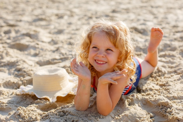 Kleines Mädchen, das am Strand auf dem Sand Sommer liegt