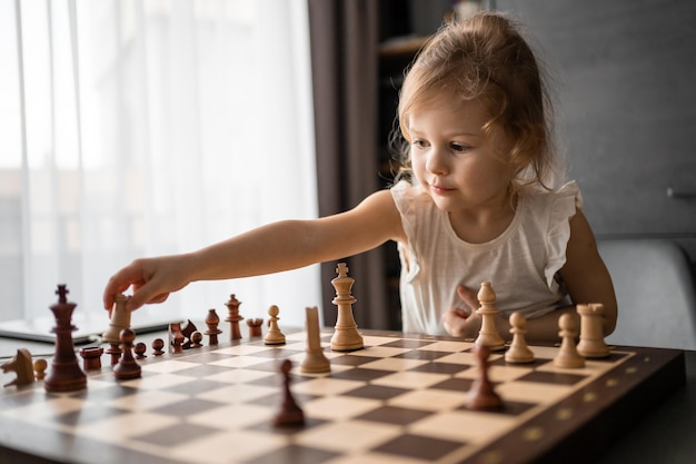 Kleines Mädchen, das am Tisch in der heimischen Küche Schach spielt, das Konzept der frühkindlichen Entwicklung und e