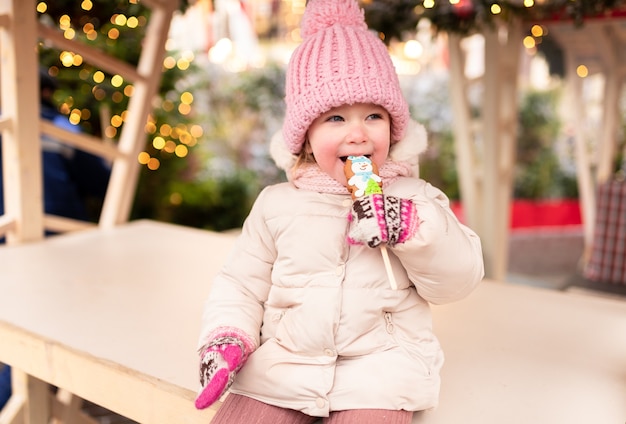 Foto kleines mädchen, das am weihnachtsmarkt sitzt und lebkuchen isst