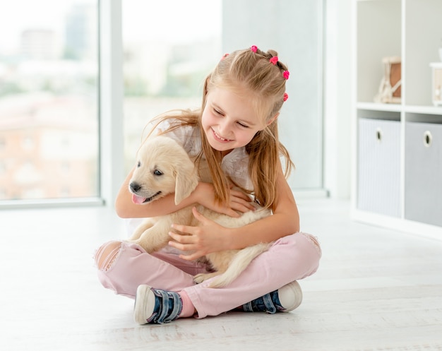 Kleines Mädchen, das Apportierhundwelpen umarmt