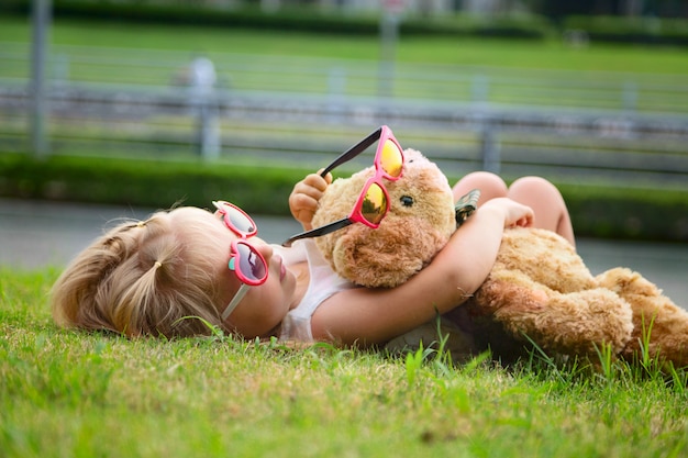 Kleines Mädchen, das auf dem Gras liegt und einen Teddybären umarmt