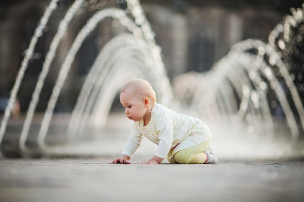 Kleines Mädchen, das auf dem Platz der Stadt in der Nähe des Brunnens kriecht