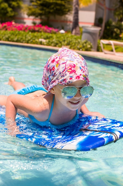 Kleines Mädchen, das auf einem Surfbrett im swimmingpoll schwimmt