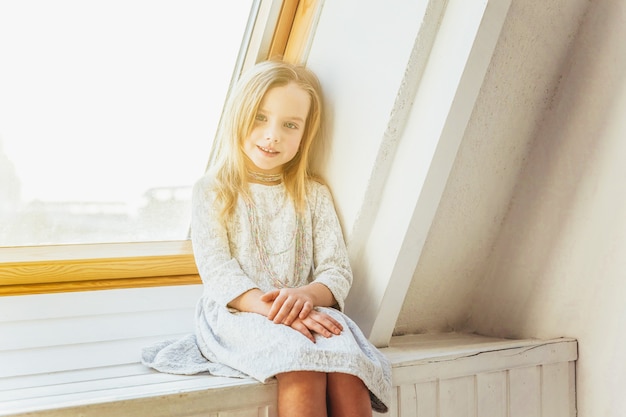 Kleines Mädchen, das auf Fensterbank im Wohnzimmer zu Hause drinnen steht