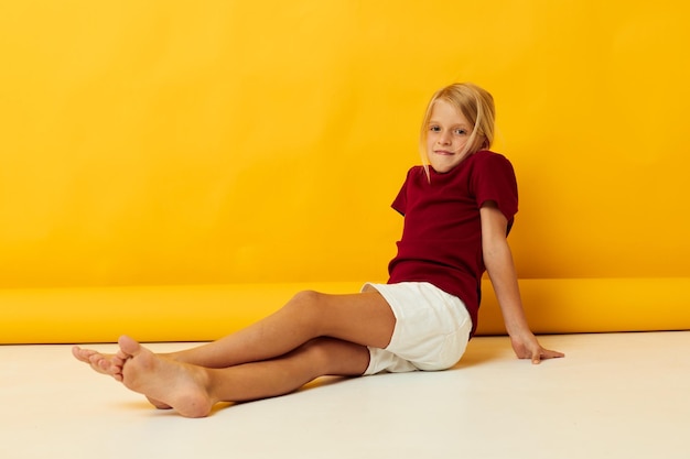 Kleines Mädchen, das auf gelbem Hintergrund auf dem Boden sitzt