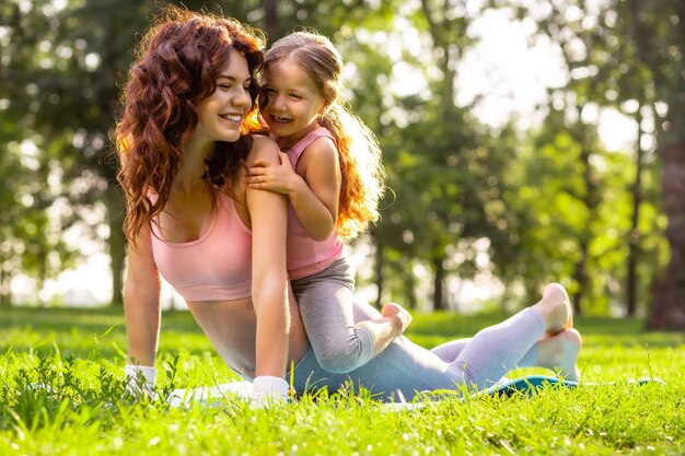 Kleines Mädchen, das auf Müttern zurück im Park sitzt