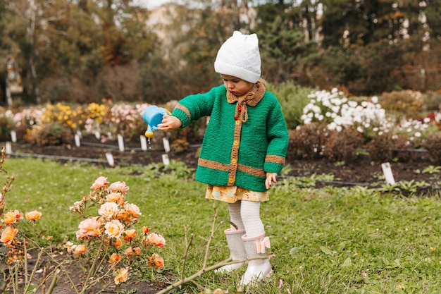 Kleines Mädchen, das Blumen mit einer Gießkanne im Garten gießt