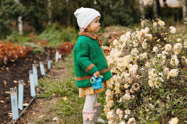 Kleines Mädchen, das Blumen mit einer Gießkanne im Garten gießt