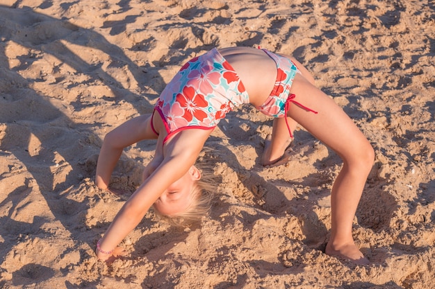 Kleines Mädchen, das Übungsbrücke auf dem Sand tut. Sommerurlaub auf See, Tourismus und Sport.