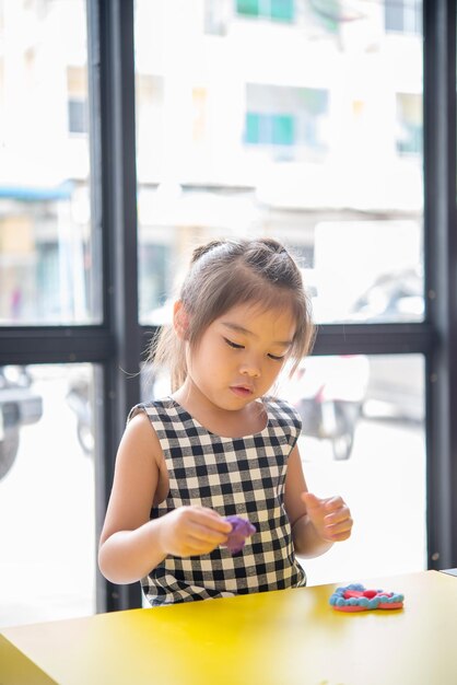 Kleines Mädchen, das bunten Ton für einige Produkte formt, denkt aus der Fantasie, glückliches Kinderspielkonzept