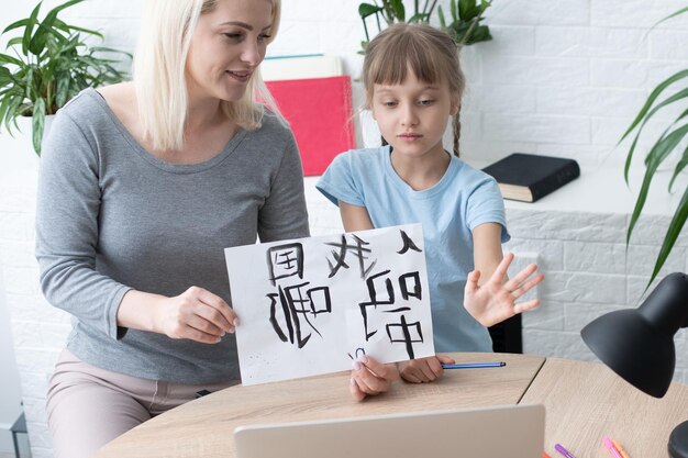 Kleines Mädchen, das Chinesisch lernt, während es seinen Laptop im Wohnzimmer zu Hause benutzt. Familienaktivitätskonzept.