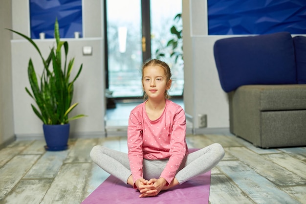 Foto kleines mädchen, das dehnübungen macht und zu hause yoga auf der fitnessmatte praktiziert