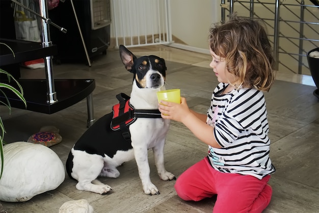 Kleines Mädchen, das dem Hund ein Getränk gibt