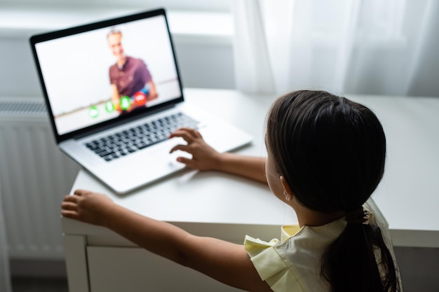 Kleines Mädchen, das den Laptopbildschirm mit überraschtem und aufgeregtem Ausdruck betrachtet. Intelligentes, lächelndes kleines Mädchen, das sich Notizen macht. Kommunikation im Geschäftskonzept.