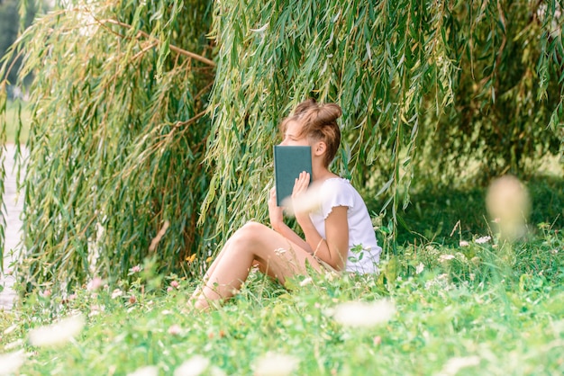 Kleines Mädchen, das ein Buch mit ihrem Freund Hündchen im Freien liest.