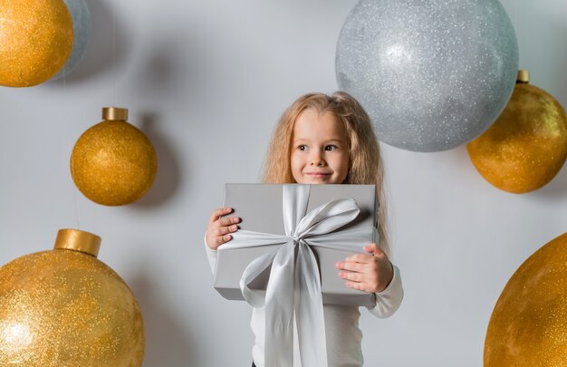 Kleines Mädchen, das ein Geschenk mit großen Weihnachtskugeln hält