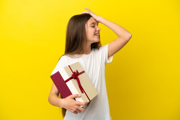 Kleines Mädchen, das ein Geschenk über isoliertem gelbem Hintergrund hält, hat etwas erkannt und beabsichtigt die Lösung