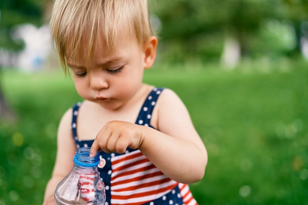 Kleines Mädchen, das eine Flasche Wasser in der Hand hält und es untersucht