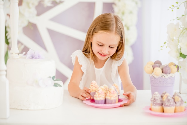 Kleines Mädchen, das eine rosa Platte mit Bonbonkuchen im Schokoriegel hält