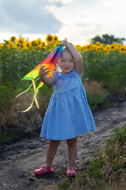 Kleines Mädchen, das einen Drachen auf einem Sonnenblumenfeld hält.