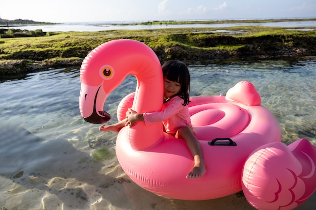 Kleines Mädchen, das einen Flamingo schwimmt, schwimmt auf dem Strand