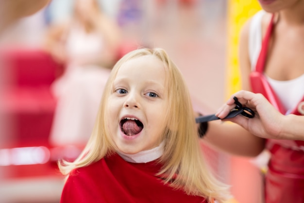 Kleines Mädchen, das einen Haarschnitt am Salon tut.