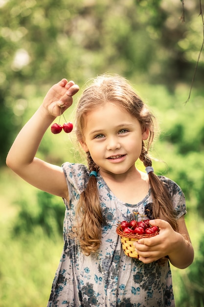 kleines Mädchen, das einen Korb der Kirschen auf Natur im Sommer hält