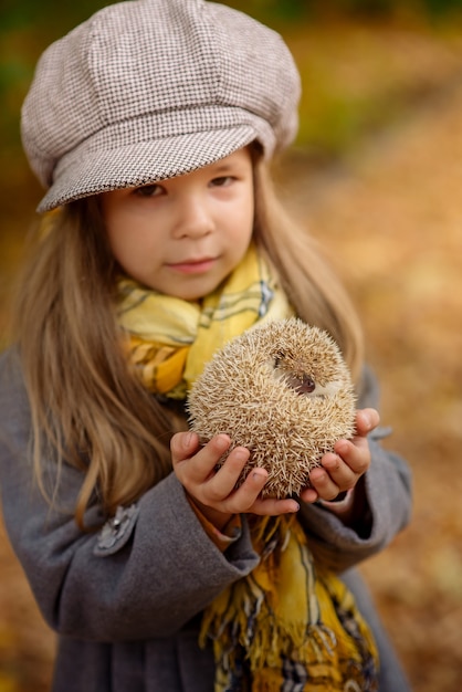 Kleines Mädchen, das einen lustigen Igel in ihren Armen im Herbst im Park hält