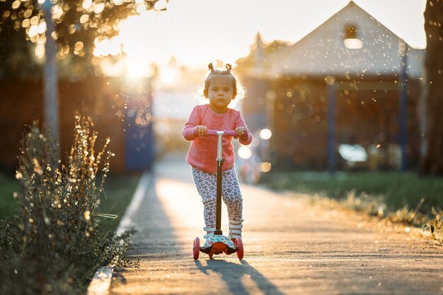 Kleines Mädchen, das einen Roller im Park reitet