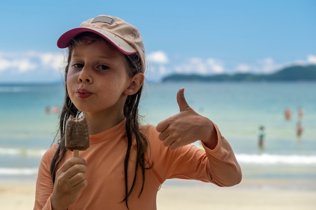 Kleines Mädchen, das Eis mit Strand im Hintergrund isst.